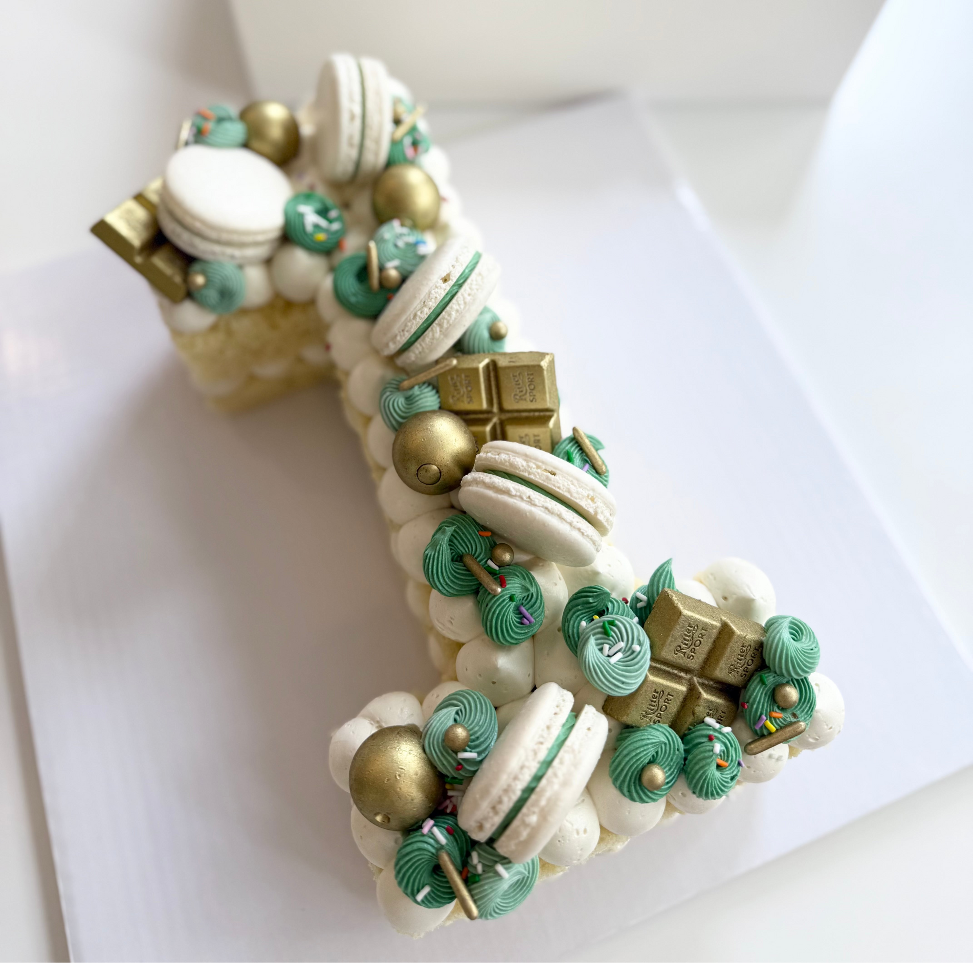 Decorative number 1 cake made of macarons with green, white, and gold colors.