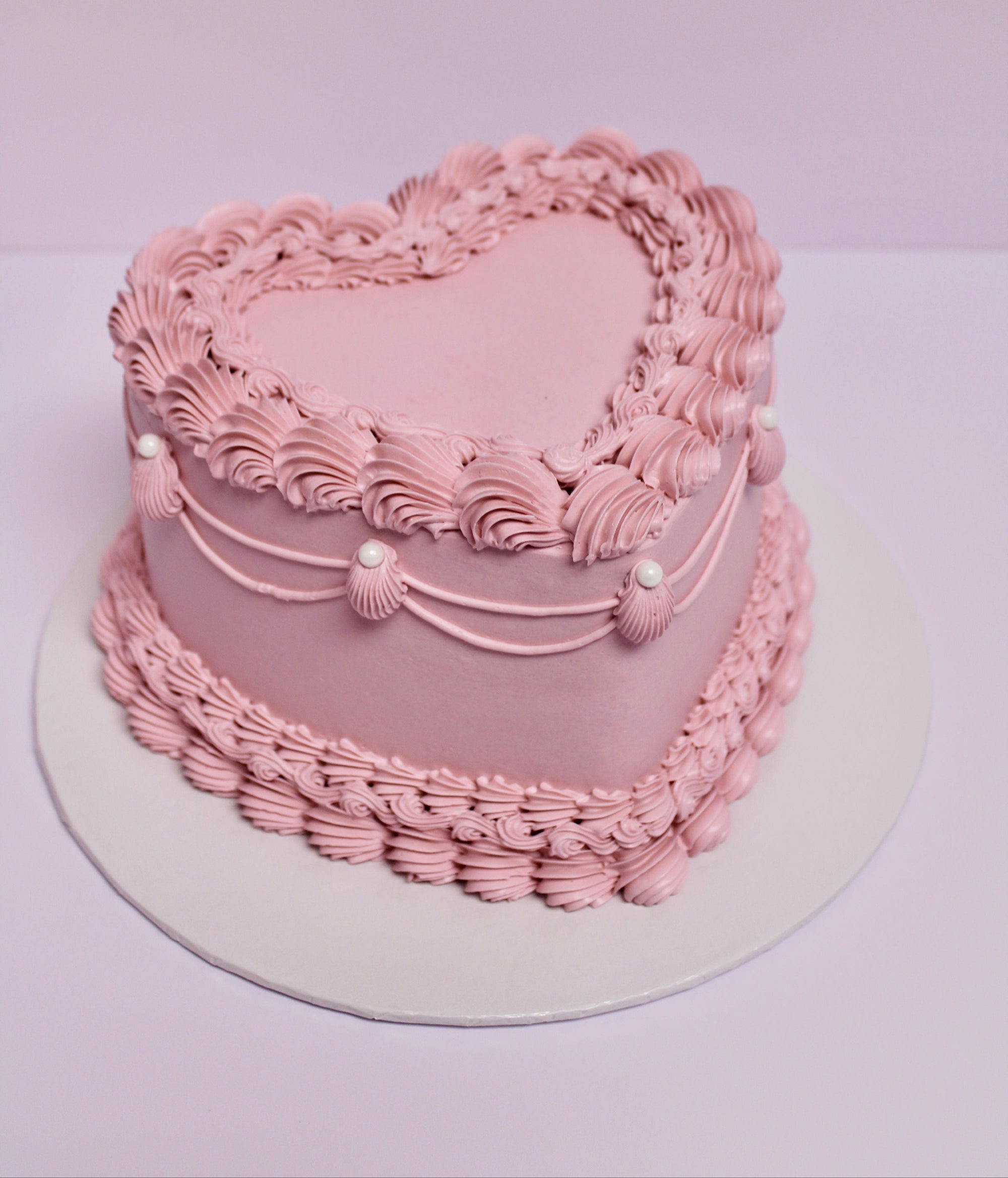 Pink heart-shaped cake with decorative icing and pearl accents