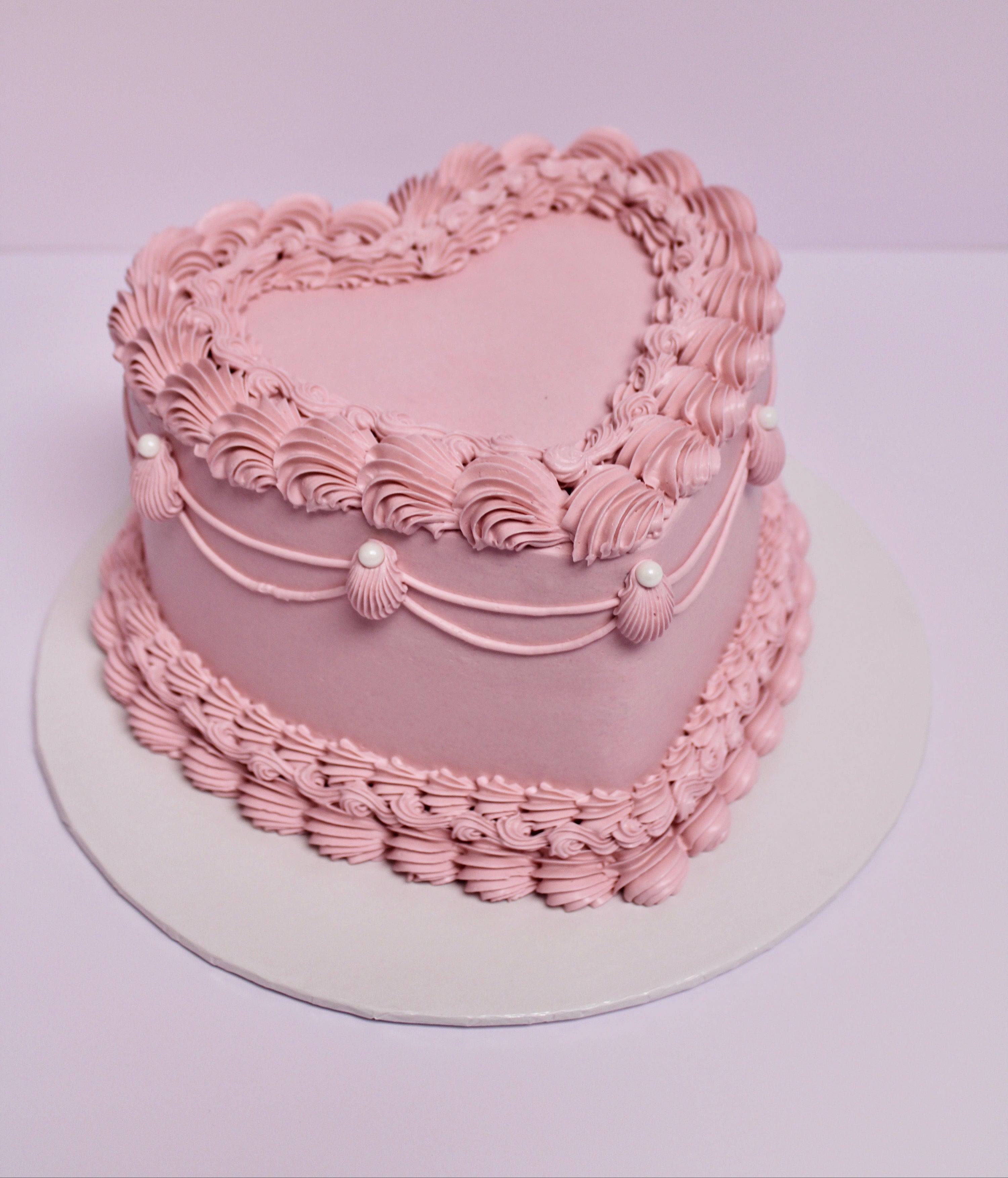 Pink heart-shaped cake with decorative icing and pearl accents