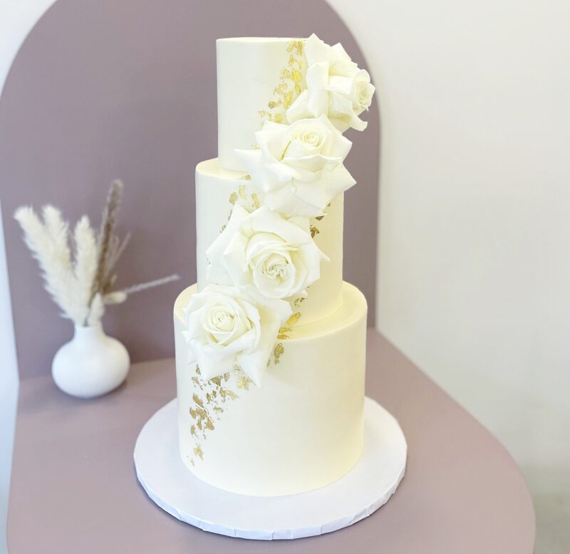 Stacked white wedding cake with fresh white roses and edible gold flakes